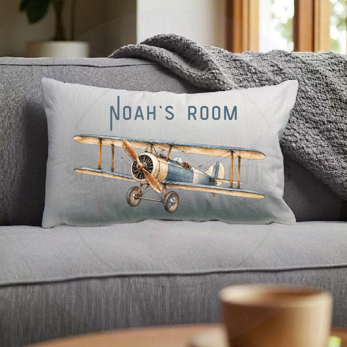 Personalised vintage biplane cushion with custom Noah's Room name displayed on grey sofa