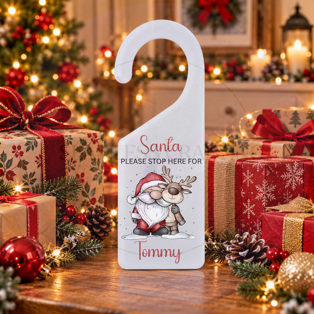 Personalised acrylic Christmas door hanger with Santa and reindeer displayed beside wrapped presents
