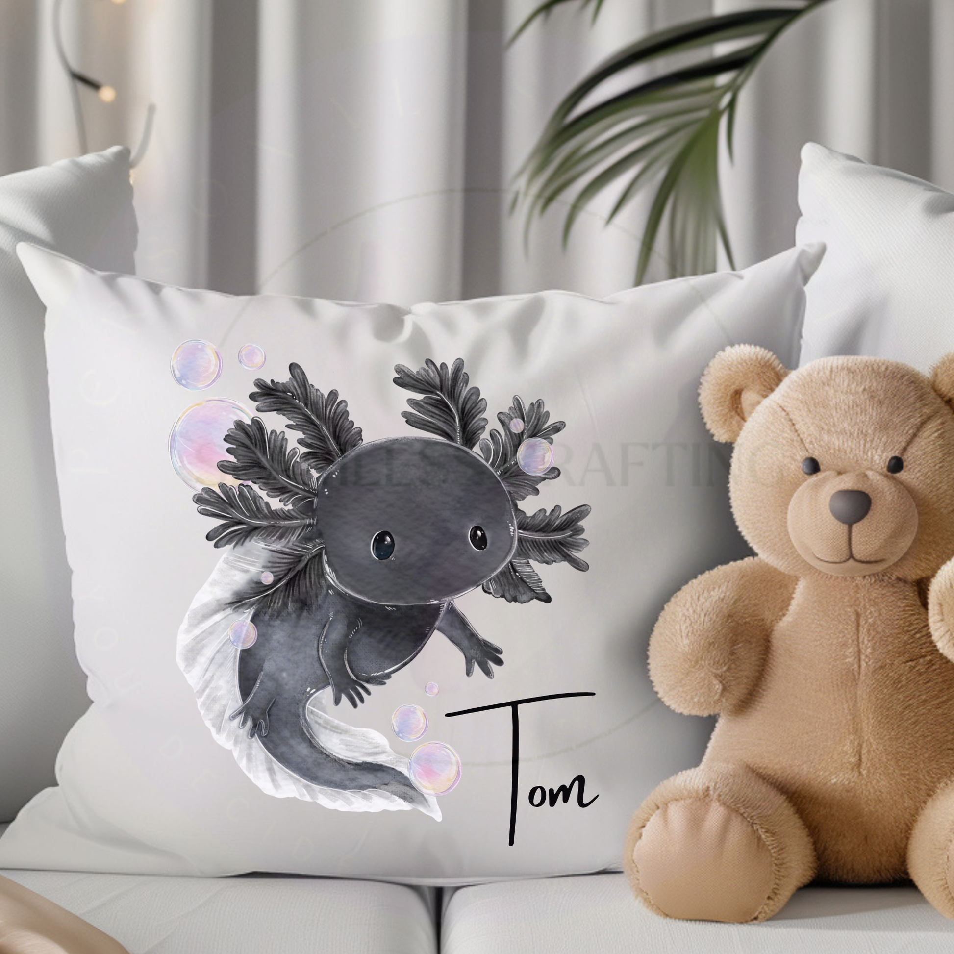 Personalised black axolotl cushion with the name Tom styled beside a teddy bear on a sofa